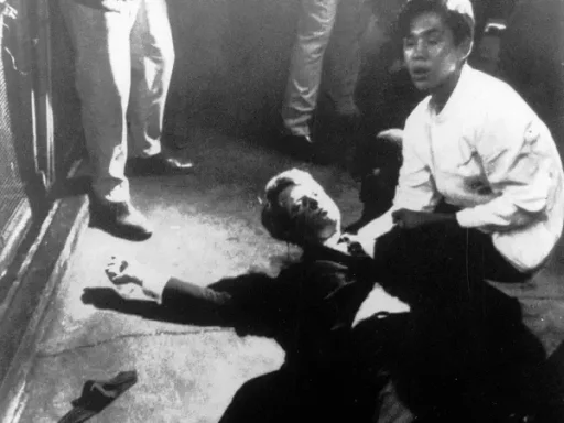 A person lies on the ground, while another kneels beside them in a tense scene.