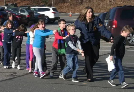 A line of children being guided by an adult in a parking lot.