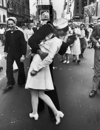 Sailor kissing a woman in a white dress on a busy street, celebrating victory.