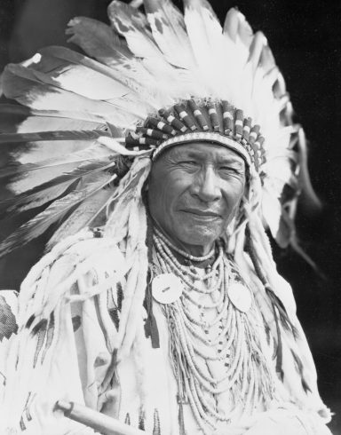 Portrait of a Native American man wearing traditional attire and a feather headdress.