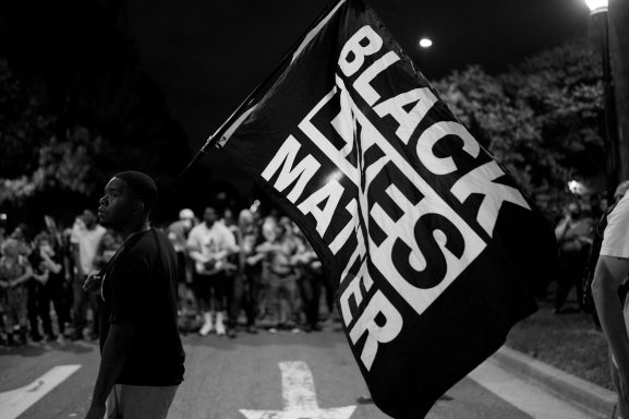 Person holding a large "Black Lives Matter" flag at a night gathering.